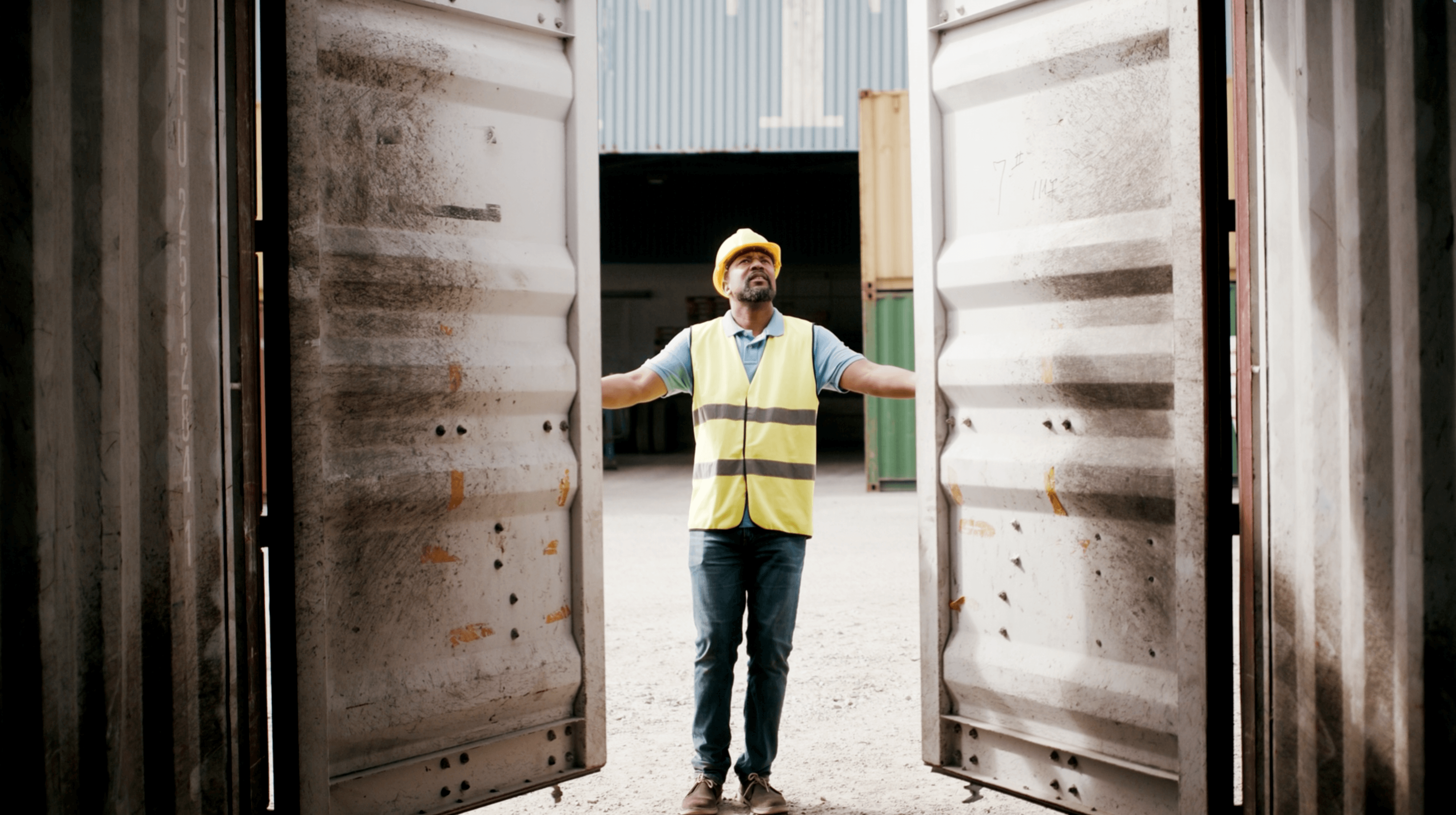 Man wearing safety vest and hard hat opening shipping container doors