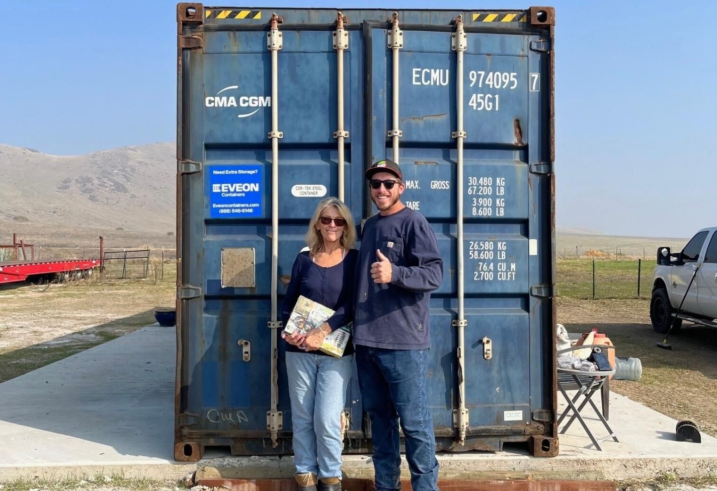 Two customers posing in front of a blue container and giving thumbs up