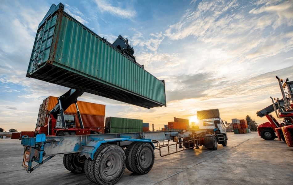 Crane picking up container to put on flatbed delivery truck