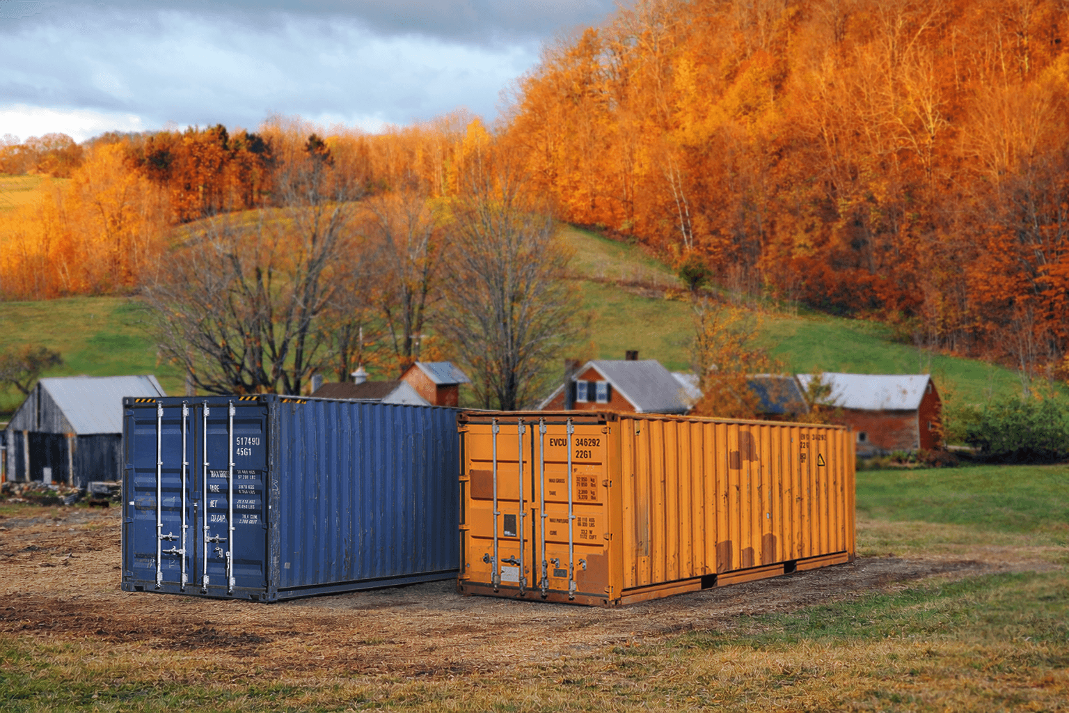 Blue and orange shipping container in front of trees with orange leaves