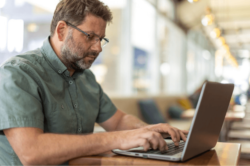 Man with glasses and green shirt typing on a laptop
