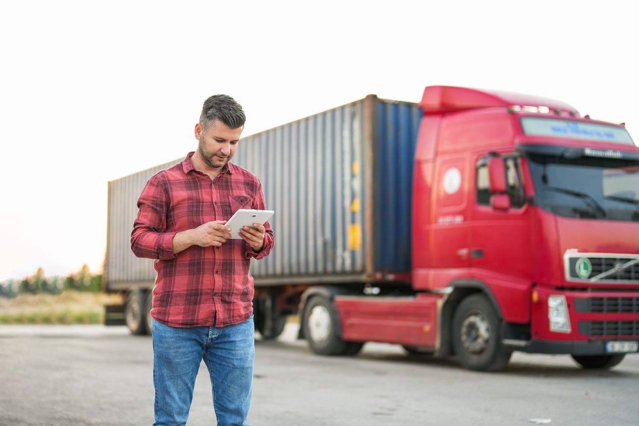 Man on iPad in front of truck hauling shipping container