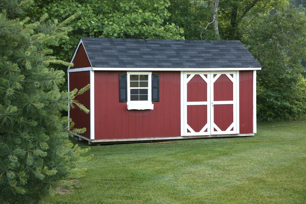 Red prefab shed with window, doors and roof on grass next to trees