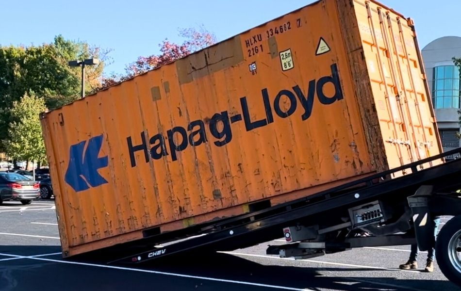Tiltbed delivery truck dropping orange container on load site