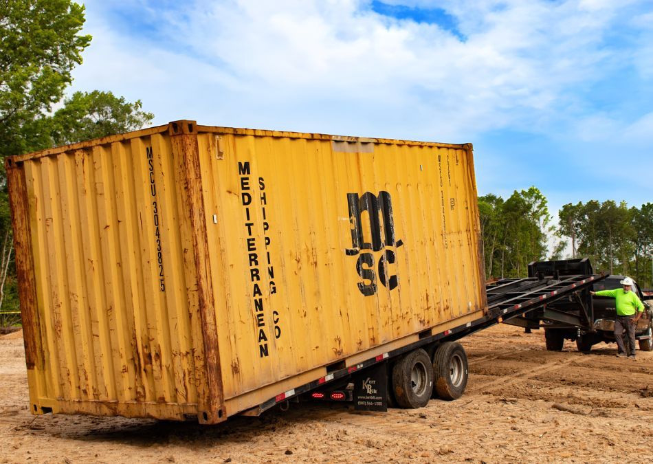 Truck putting a yellow container on dirt with tilt bed delivery
