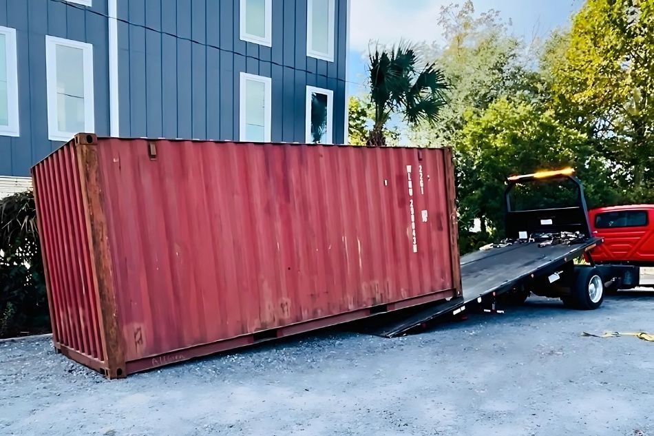 Tiltbed delivery truck dropping a red container at delivery site