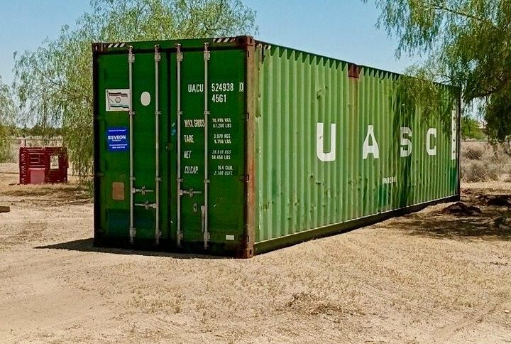 Green 40ft shipping container in dirt field